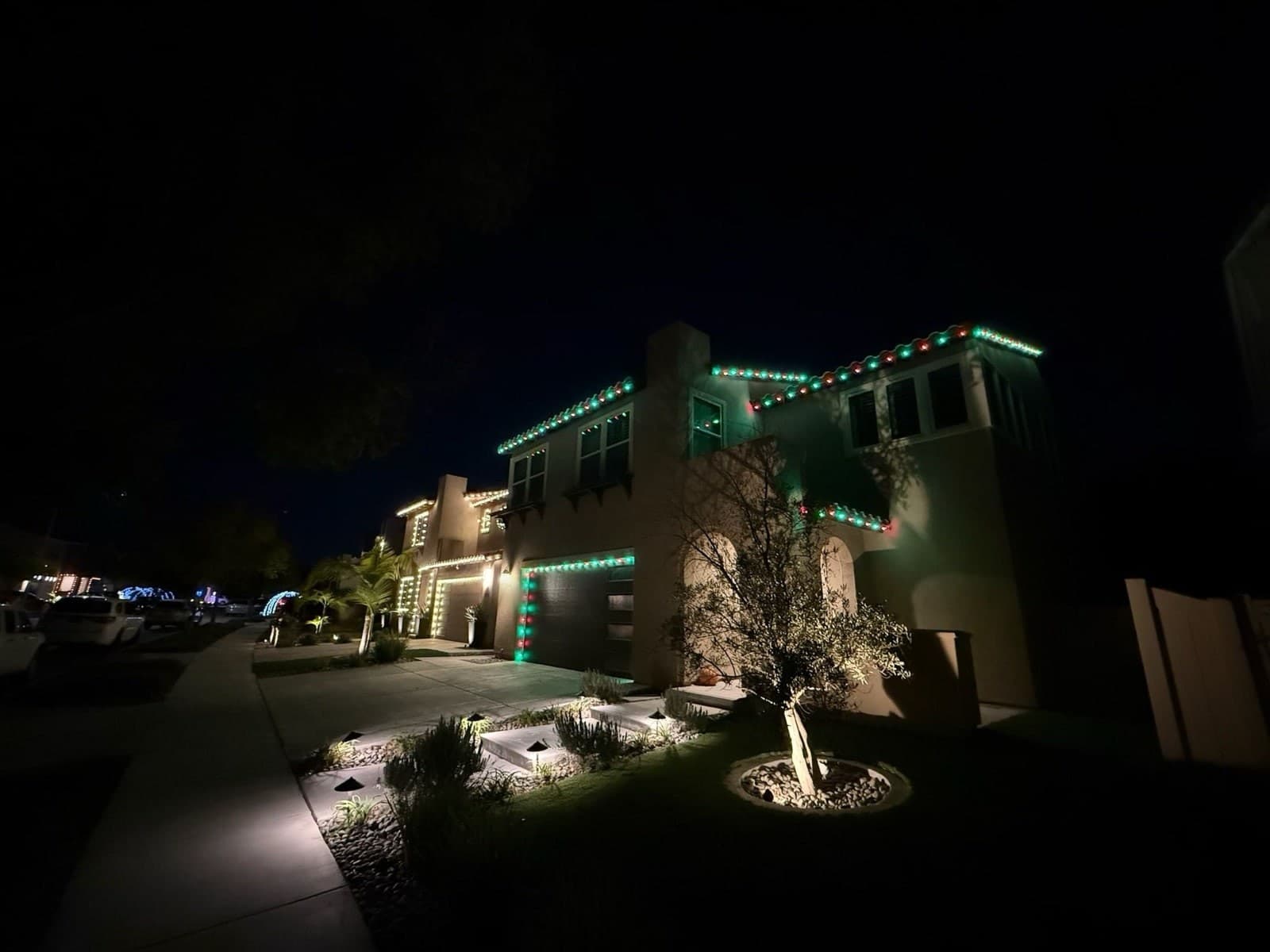 Red and green C9 Christmas lights tracing the tile roofline and garage of a two-story San Diego home at night