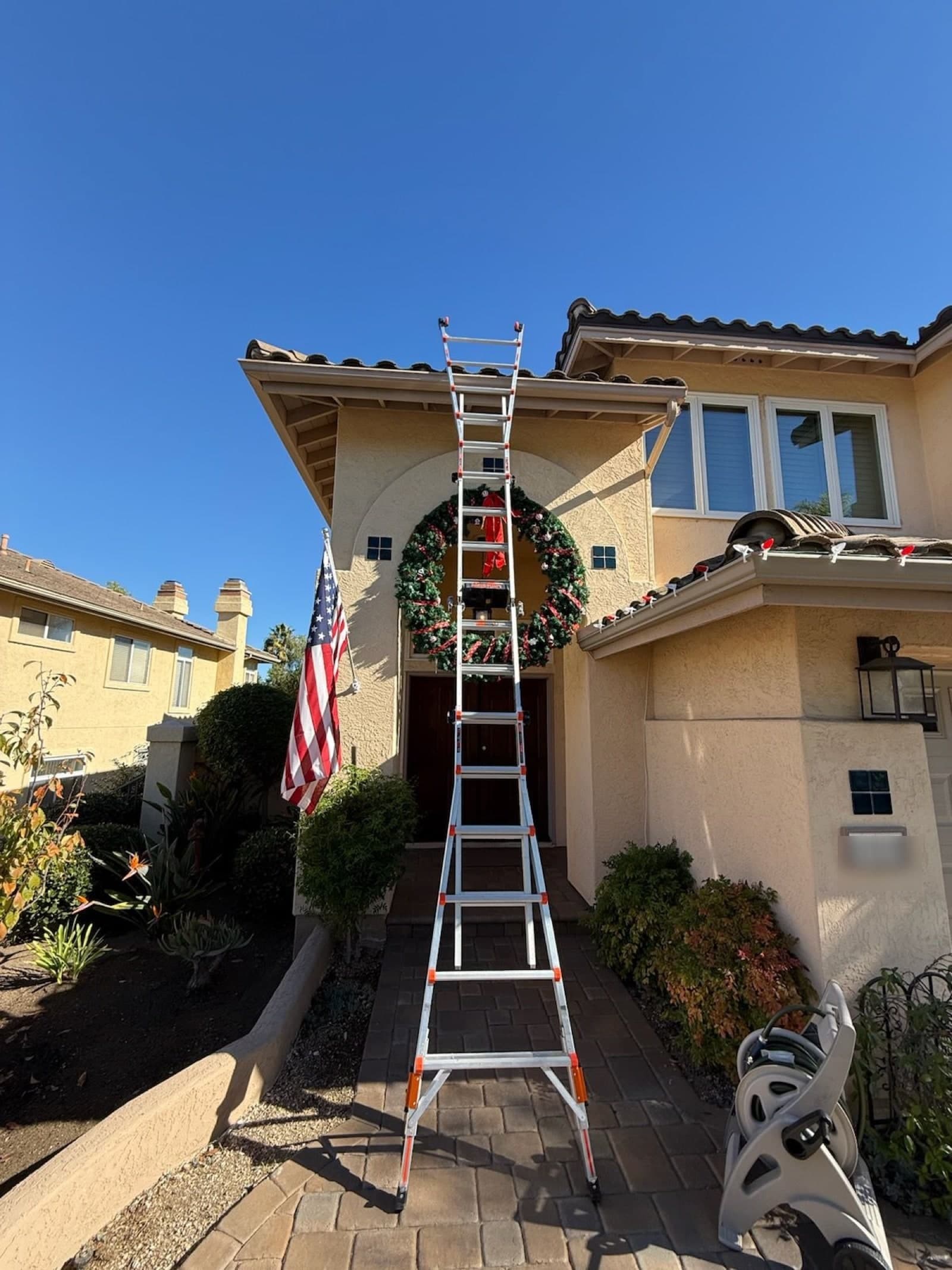 A lit wreath and garland being installed over the entry of a San Diego County home